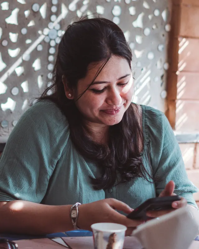 Mulher sentada à mesa, sorrindo de leve para o celular.