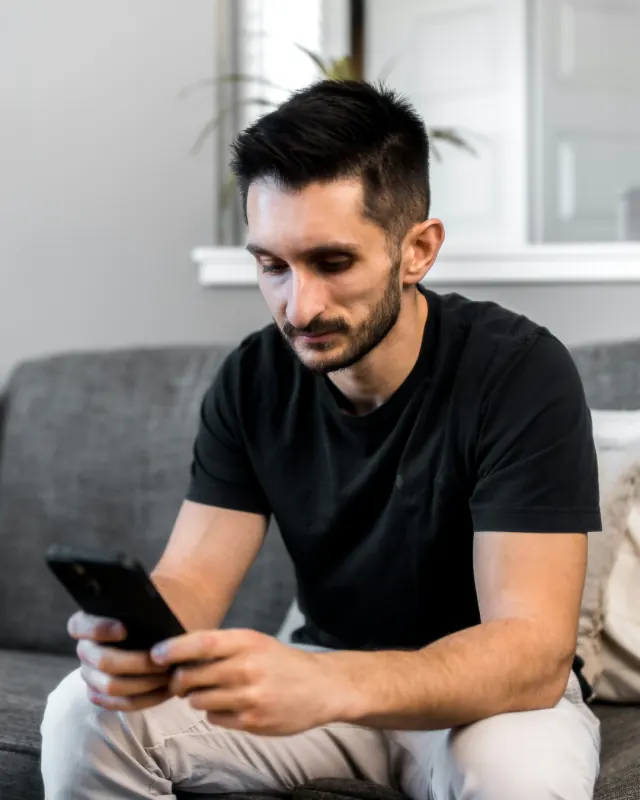 Homem sentado no sofá, olhando o celular com calma.