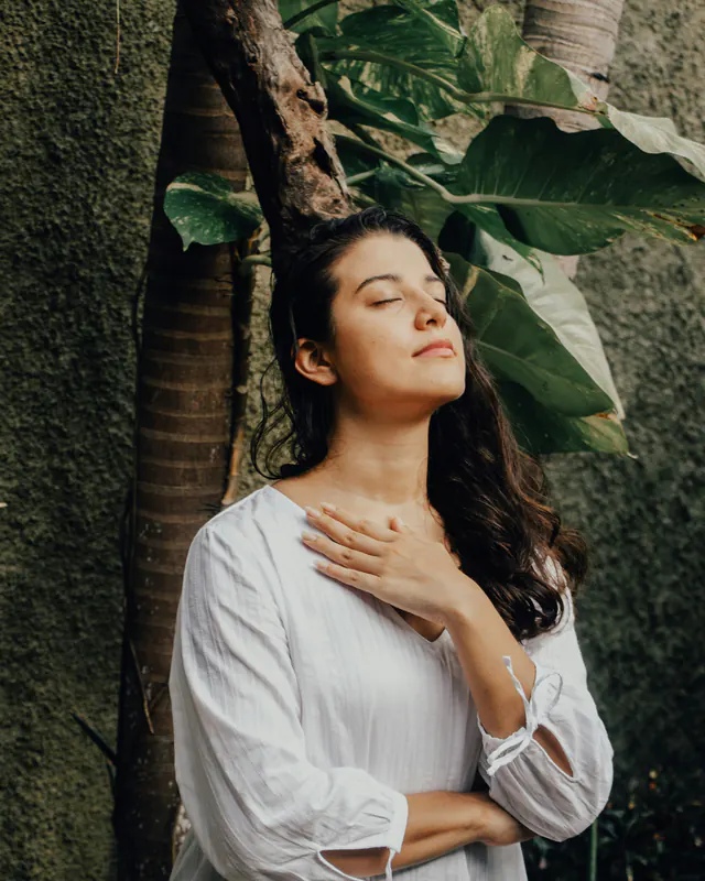 Mulher de olhos fechados, com a mão no peito, respirando com calma.
